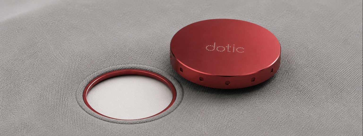 A red aluminium dotic module beside its magnetic ring port sewn into grey fabric